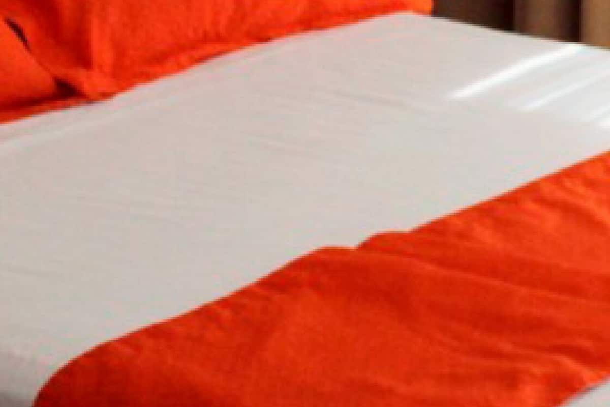 A bed with white and orange bedding, a black side table, and a beige curtain.