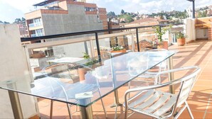 Mesa de vidrio con sillas de metal en una terraza con vistas a edificios y a un paisaje urbano.