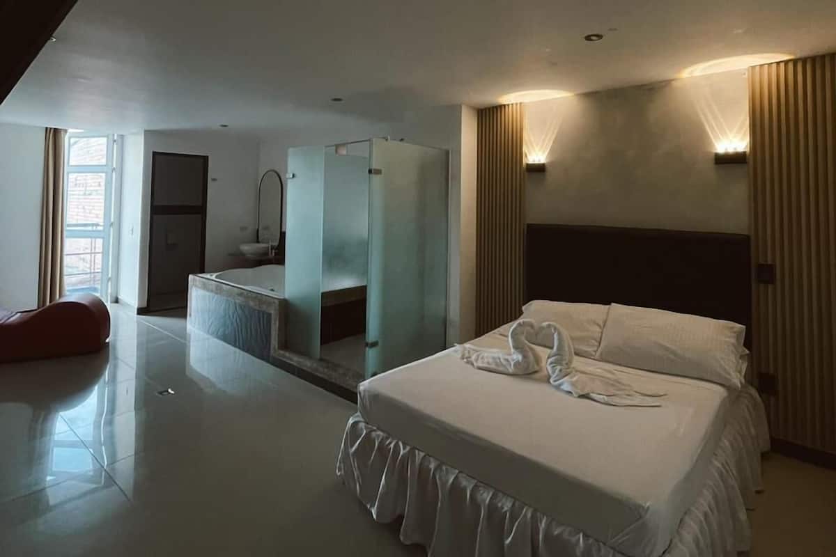 A modern hotel room with a large bed, a separate bathroom, and a view of the outside.