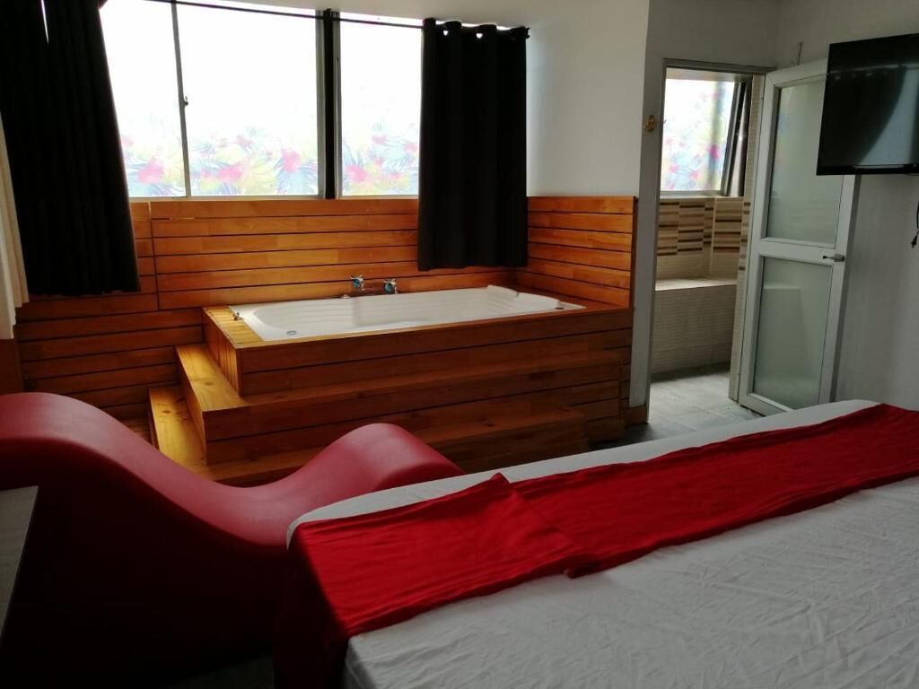 A room with a wooden bench, a red chair, a large bathtub, and a TV on the wall.
