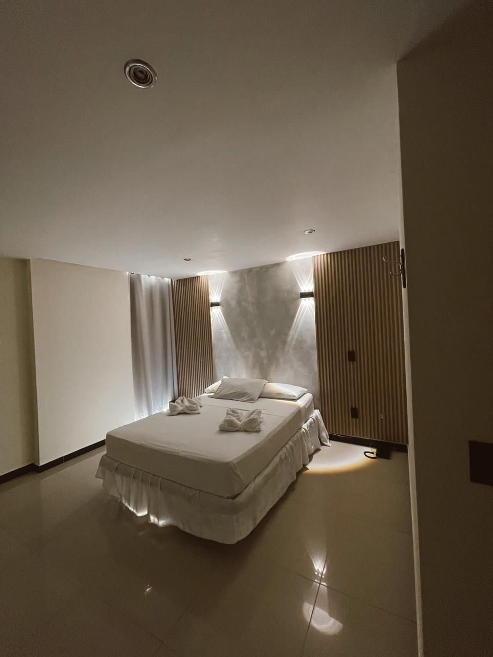A modern bedroom with a large bed, a ceiling light, and a wall-mounted panel.