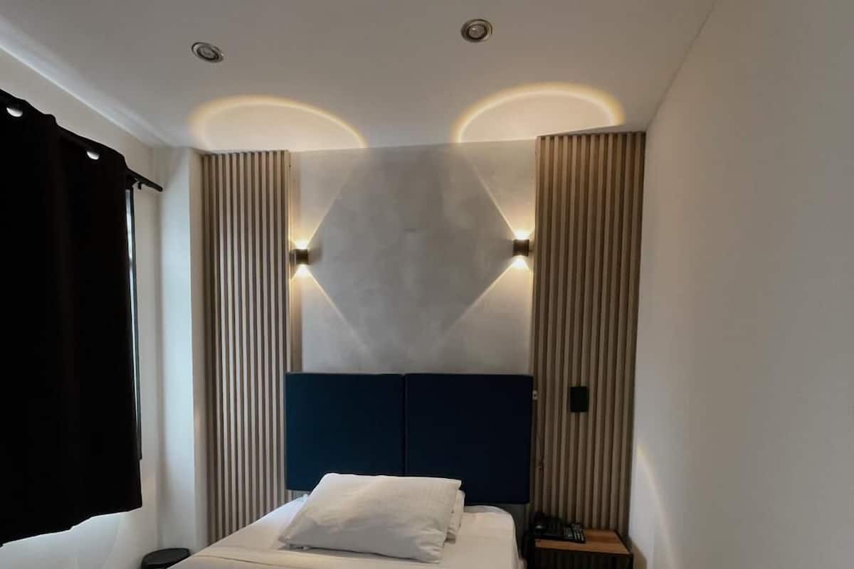 A hotel room with a large bed, a nightstand, and a headboard with wall sconces.