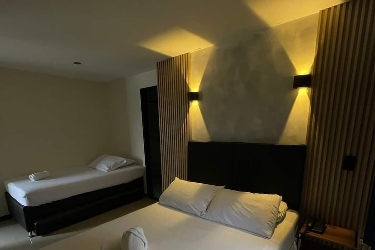 A hotel room with a large bed, a smaller bed, and a bedside table with a lamp.