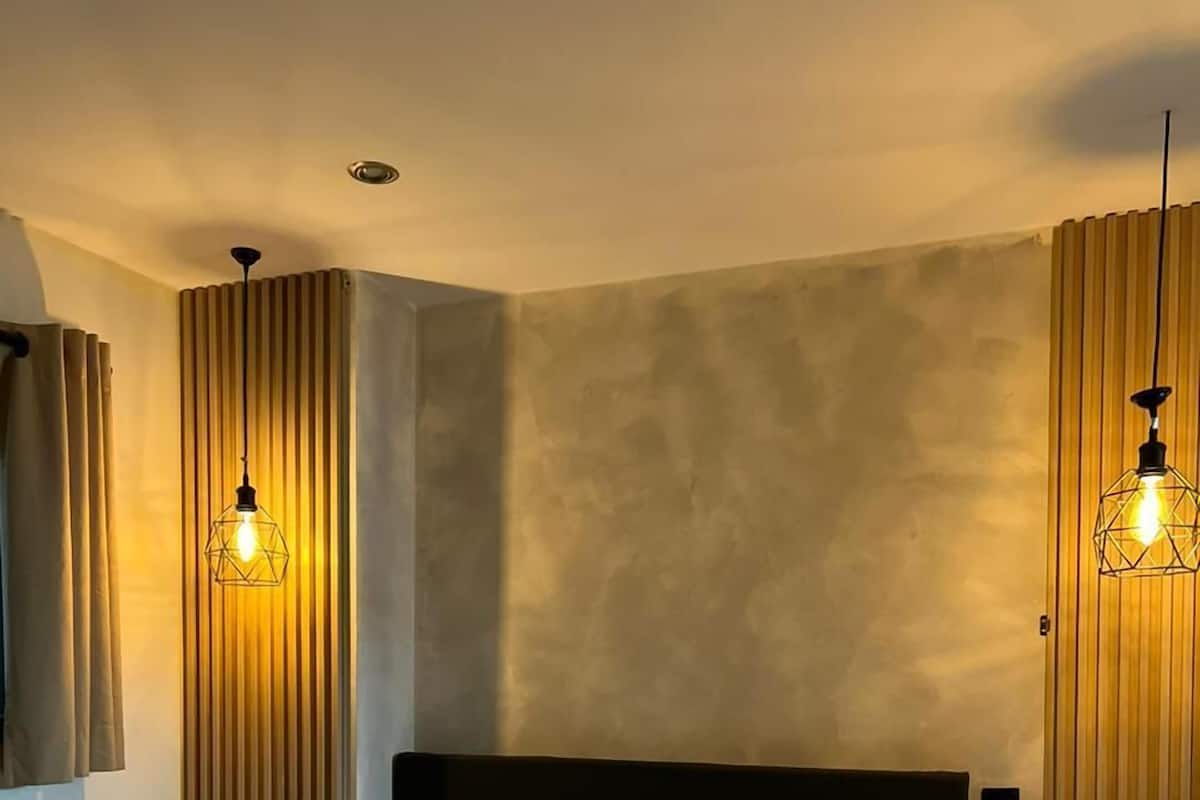 A hotel room with a large bed, two bedside lamps, a telephone, and a wall-mounted thermostat.