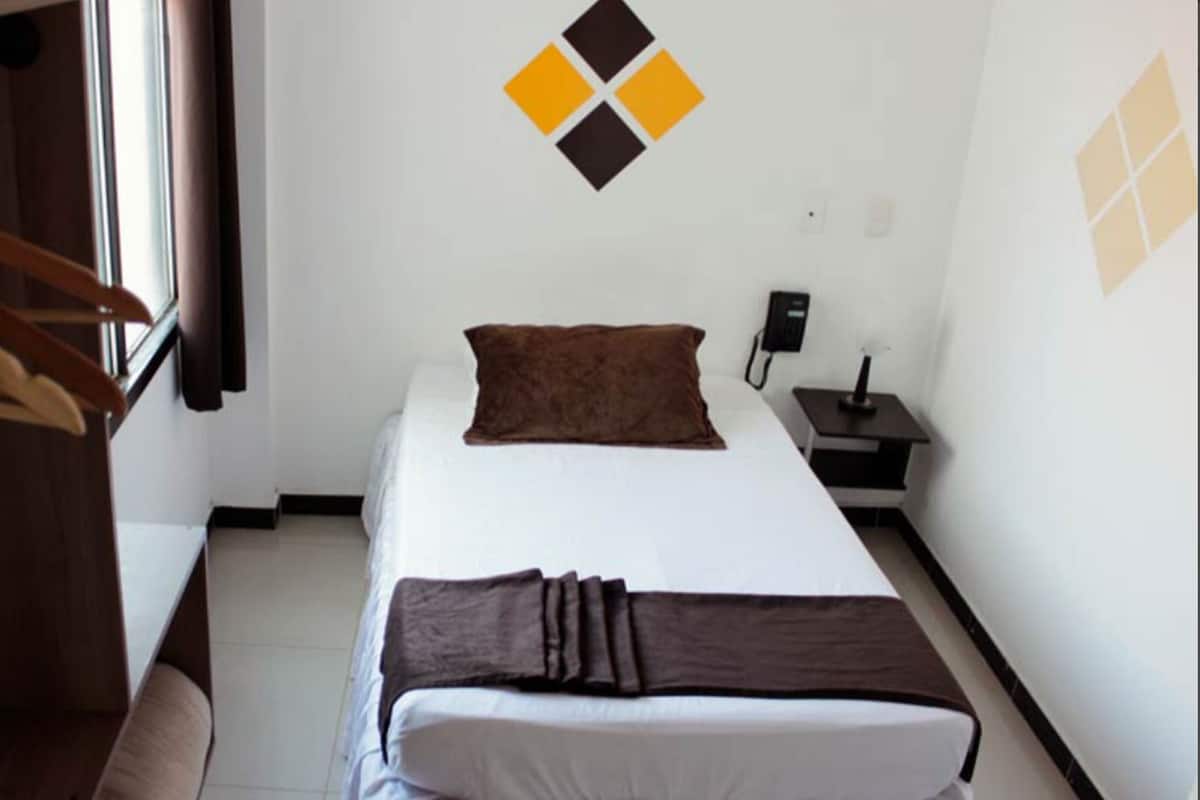 A hotel room with a bed, a nightstand, a telephone, and a coat rack.