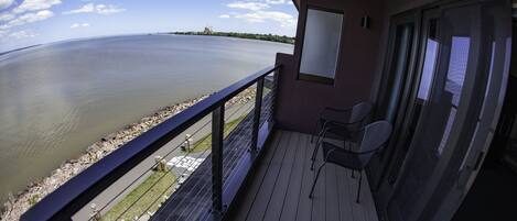 A balcony with a view of a calm body of water, a chair, and a window.