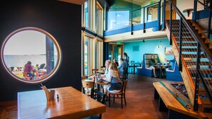 A restaurant with a large round window overlooking the sea, wooden tables and chairs, and a staircase leading to an upper level. - Blue Wave Inn (Ashland)