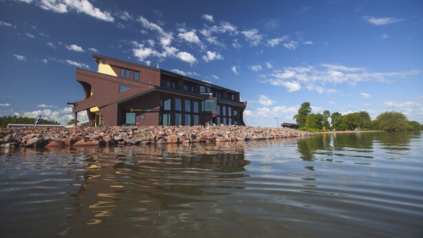 A modern building with a unique architectural design, situated on a rocky shoreline with a body of water in the foreground. - Blue Wave Inn (Ashland)