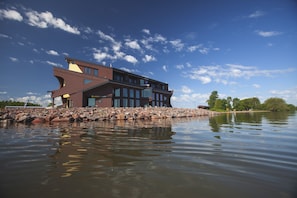 A modern building with a unique architectural design, situated on a rocky shoreline with a body of water in the foreground. - Blue Wave Inn (Ashland)