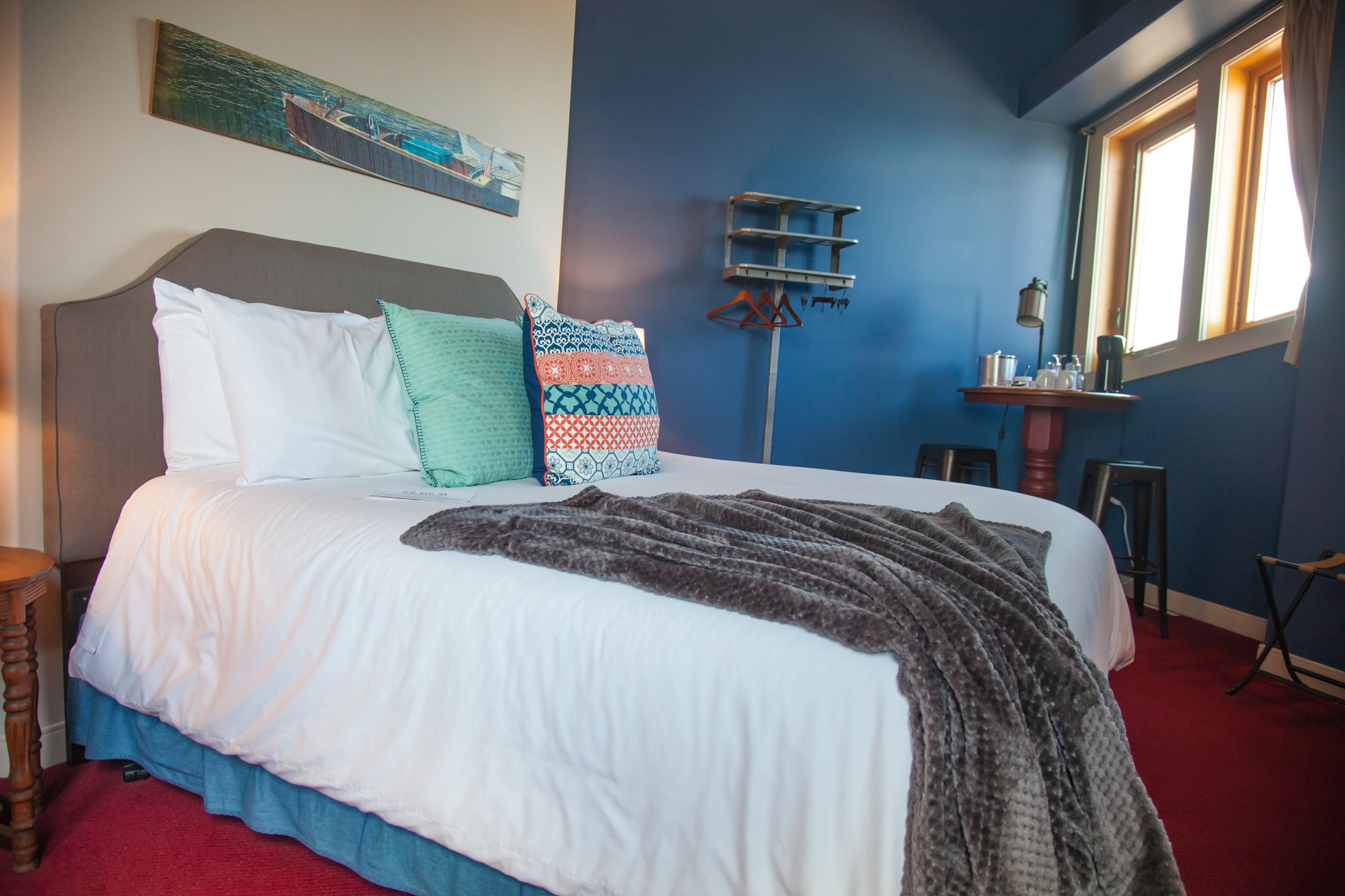 A neatly made bed with white and patterned pillows, a grey blanket, and a red carpeted floor.