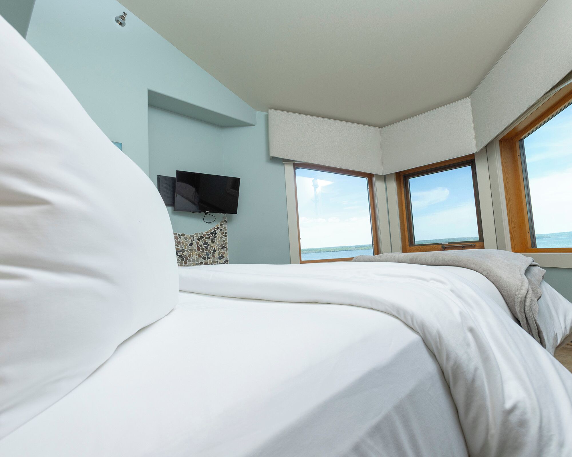 A bedroom with a bed, a television mounted on the wall, and a window providing a view of the sea.