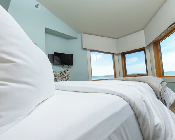 A bedroom with a bed, a television mounted on the wall, and a window providing a view of the sea. - Blue Wave Inn (Ashland)
