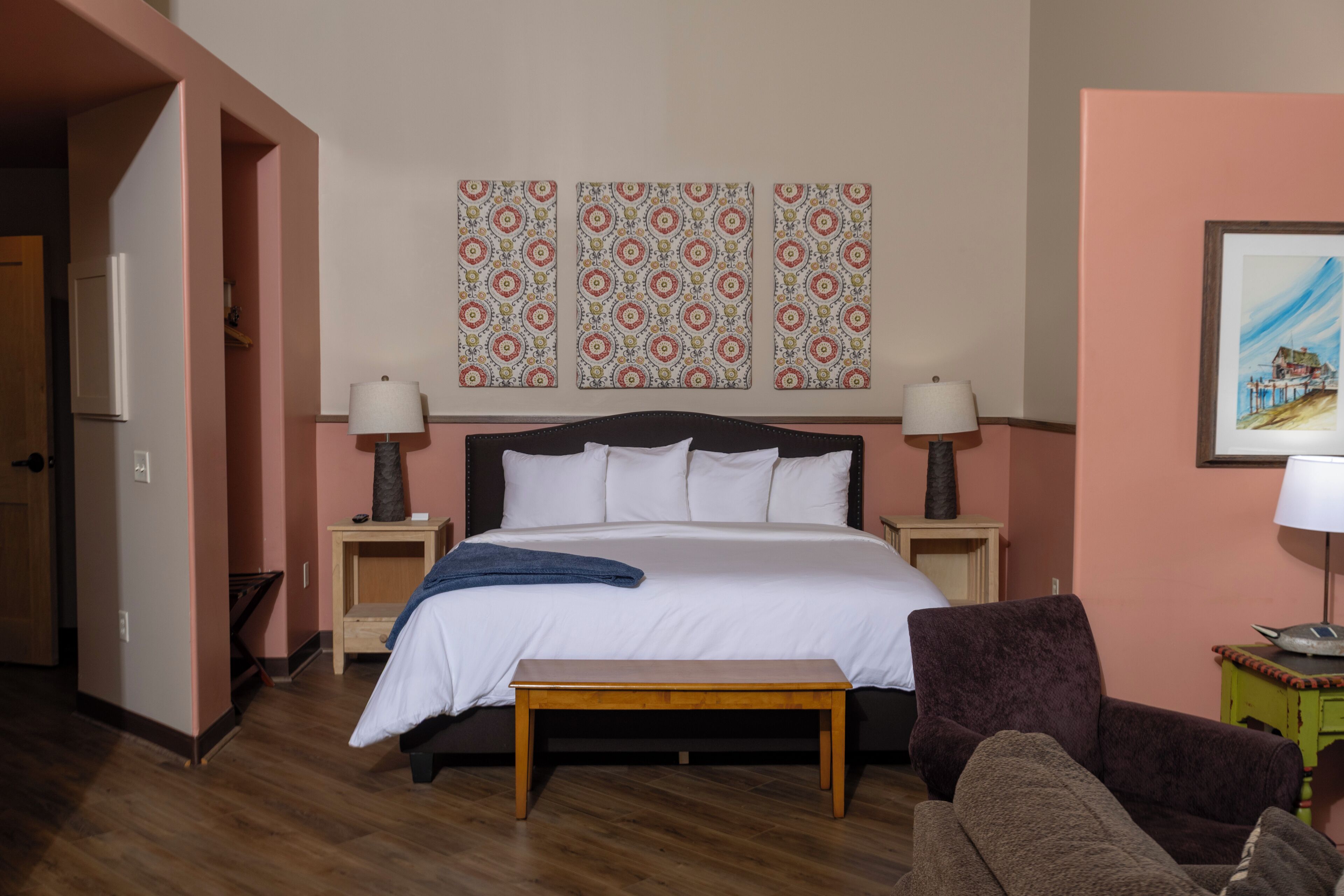 A bedroom with a bed, bedside tables, a bench, a chair, and patterned wall art.
