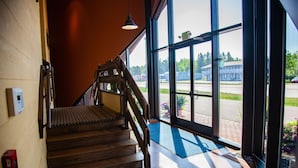 A wooden staircase leading to a bright room with large windows and a view of a parking lot. - Blue Wave Inn (Ashland)