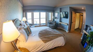 Habitación de hotel con una cama grande, un escritorio con lámpara, un televisor y una puerta corredera que da a un balcón.