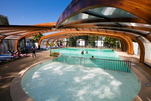 A swimming pool with a wooden canopy overhead, surrounded by lounge chairs and a few people. - Le Domaine de la Marina (Messanges)