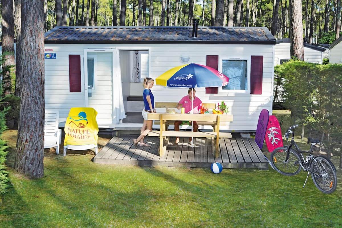Una casa móvil con un muelle de madera, una mesa de picnic y una bicicleta.