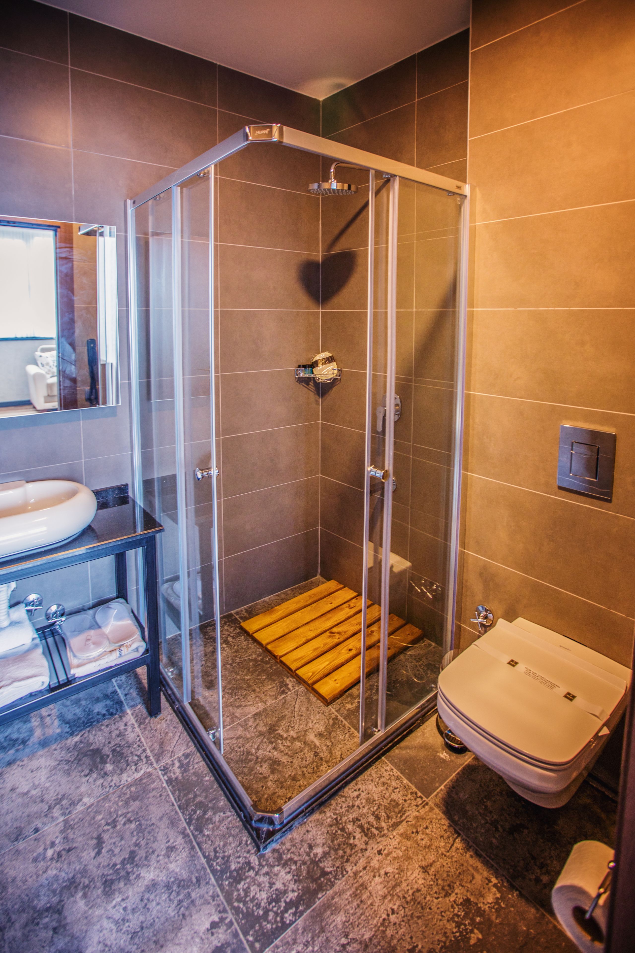 Eine Dusche mit Glastür, eine Holzbank und eine Toilette.