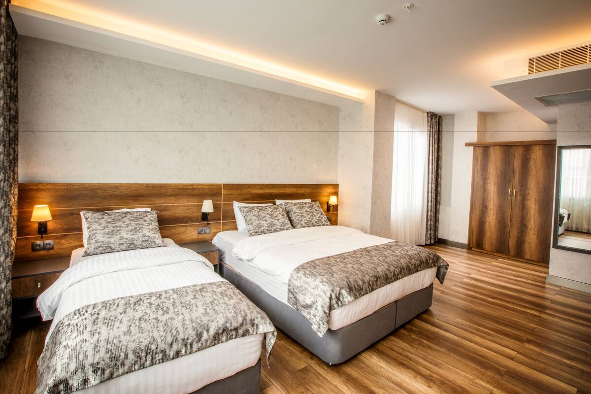 A modern hotel room with two beds, wooden flooring, and a large mirror.