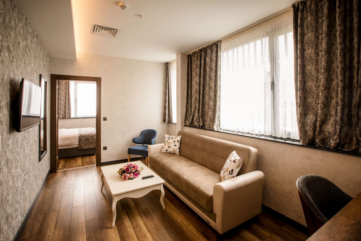 A modern living room with a sofa, a coffee table with flowers, a chair, and a bed in the background.