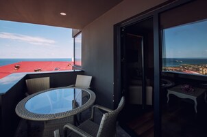 Un balcone con un tavolo in vetro e sedie in vimini, affacciato su una città costiera.