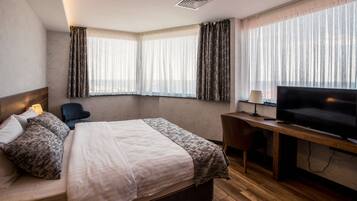 Una habitación de hotel con cama, escritorio con televisor y dos ventanas con cortinas.
