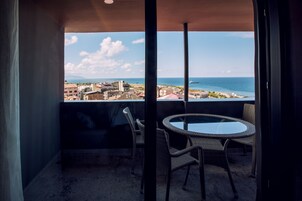 Un balcón con puerta de vidrio, sillas de mimbre y una mesa redonda.