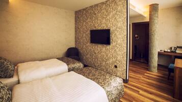 A hotel room with two beds, a television mounted on the wall, a wooden floor, and a bathroom visible through an open door.