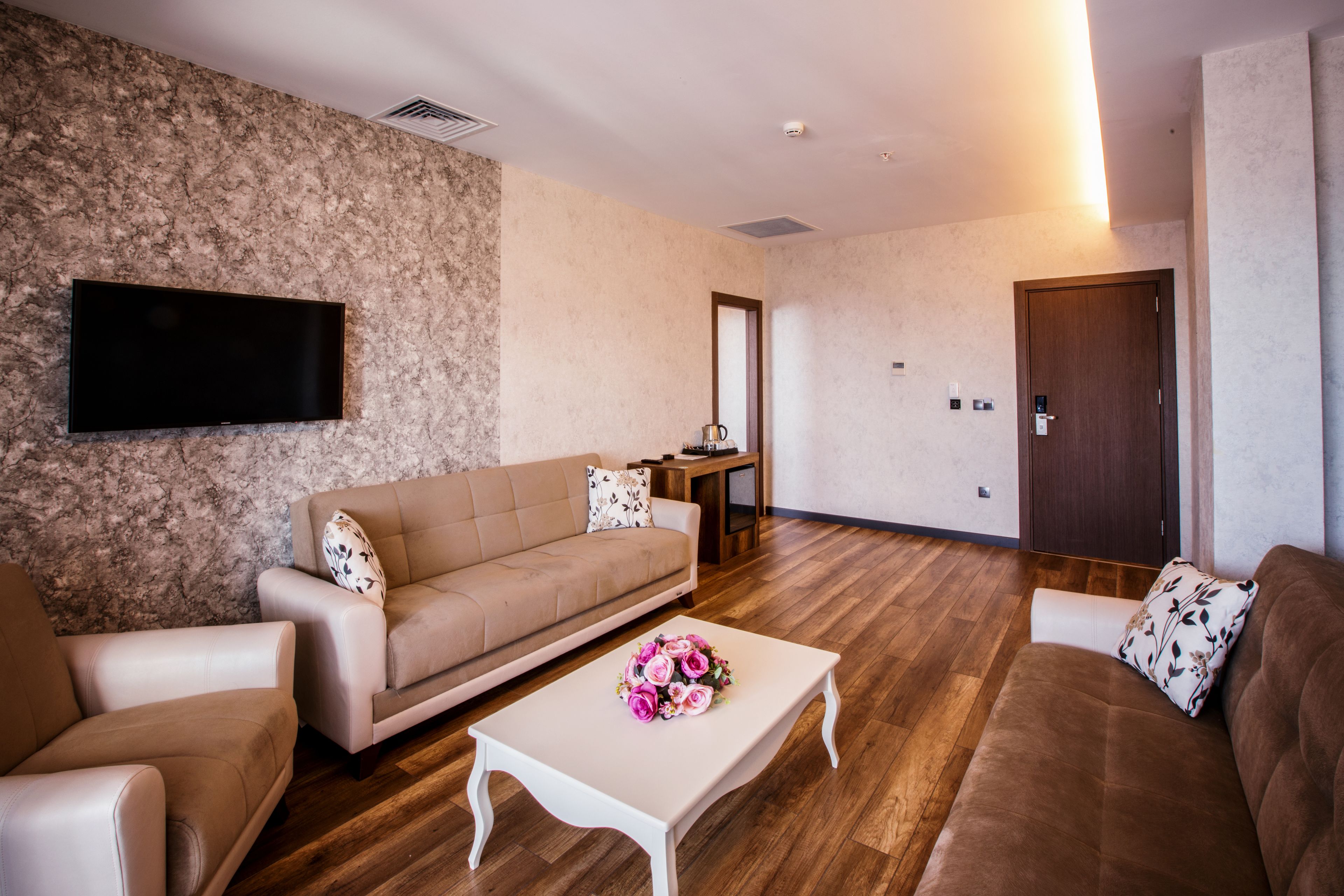 A living room with a sofa, a coffee table with flowers, a flat-screen TV, and a wooden door.
