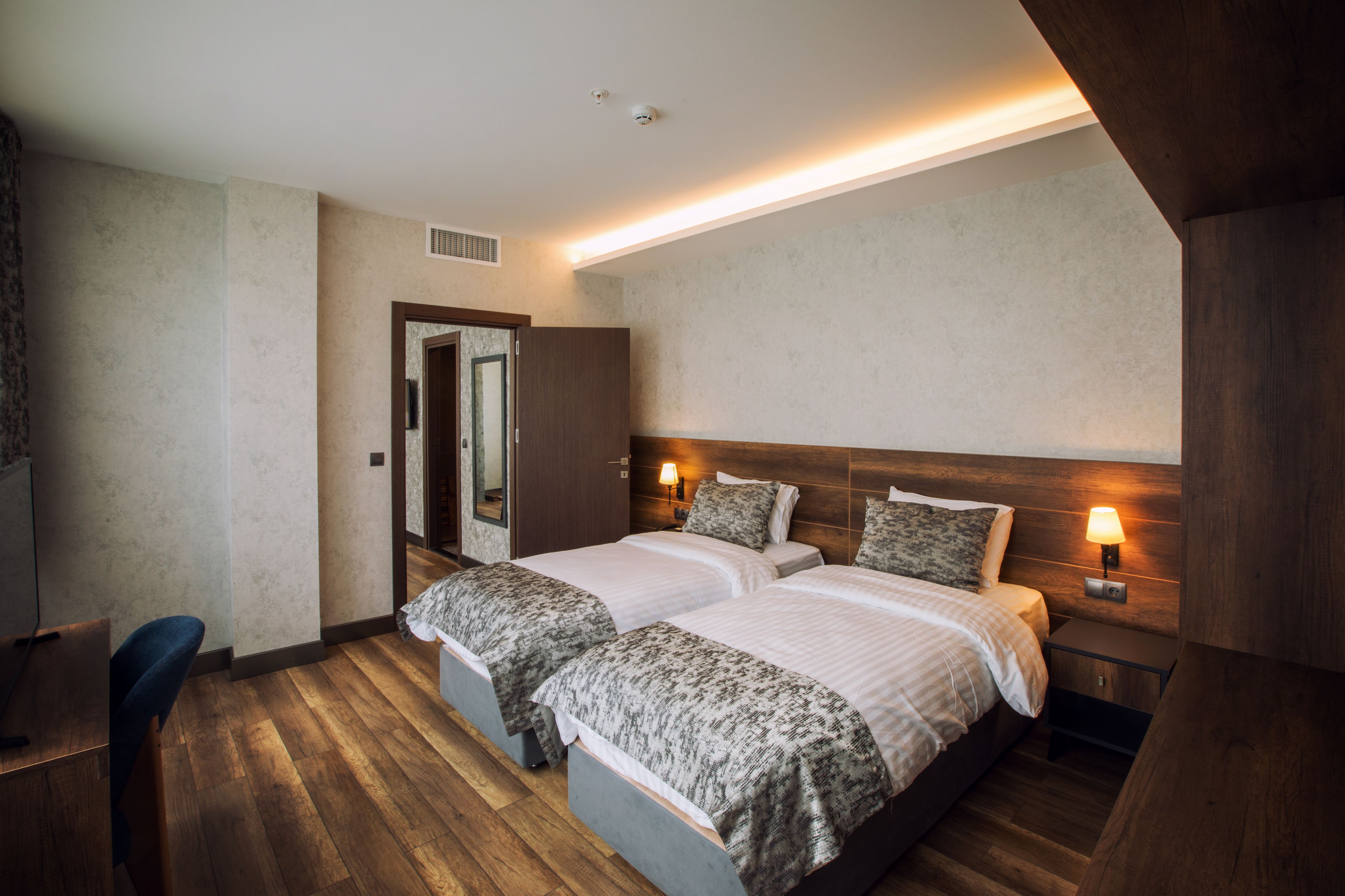 A hotel room with two beds, wooden flooring, a desk, and a mirror.