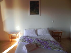 Ein Schlafzimmer mit einem Bett, zwei Nachttischen, einem Bild an der Wand und einem Fenster.