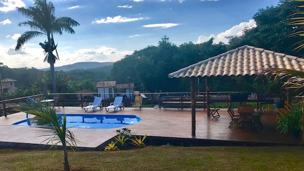 A pool area with a tiled roof, lounge chairs, and a view of a mountainous landscape. - Pousada Estancia do Vale (Jaboticatubas)