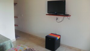 A room with a television on a wall-mounted shelf, a small black refrigerator, and a bed with a floral bedspread. - Pousada Estancia do Vale (Jaboticatubas)