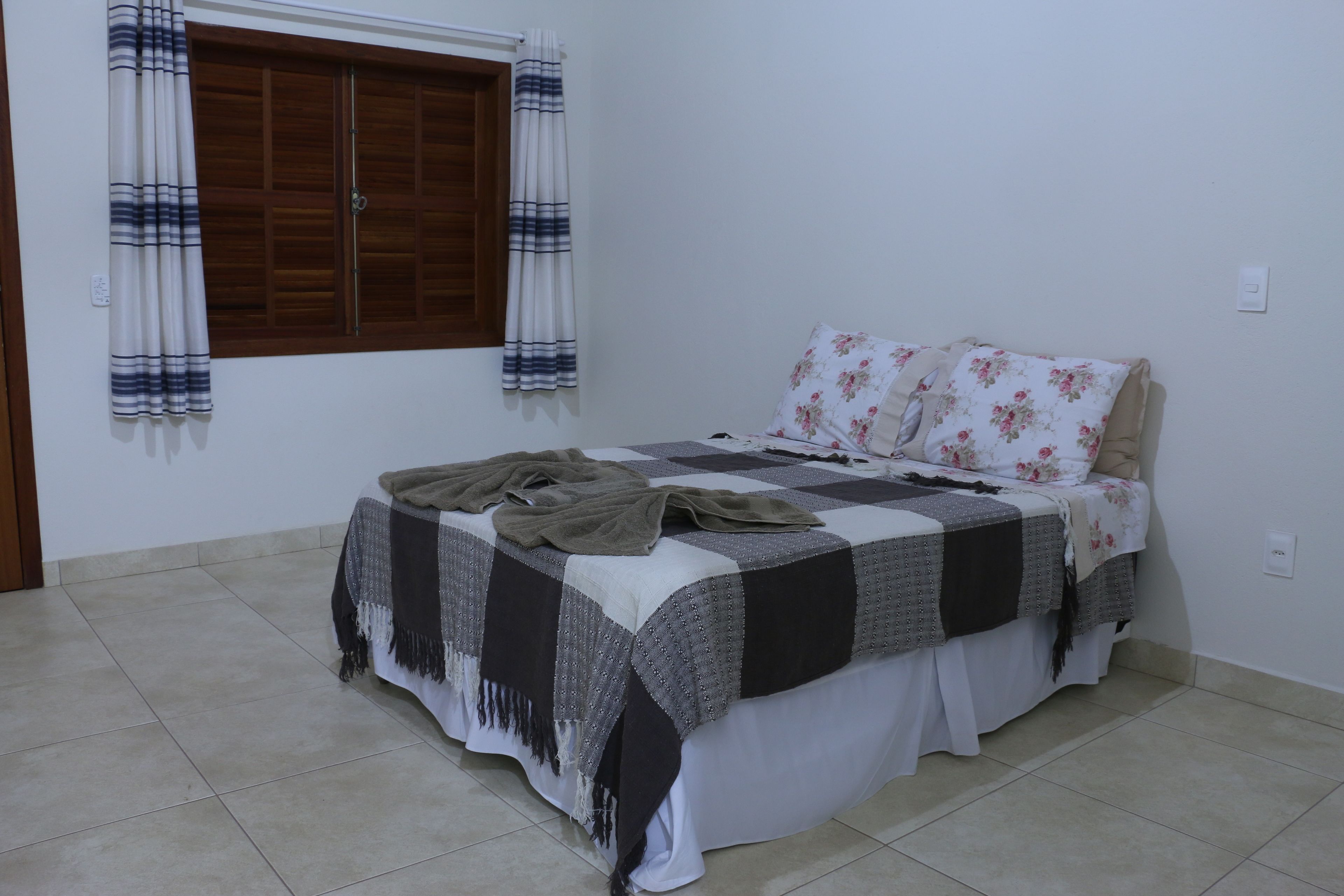 A bedroom with a bed, curtains, and a window. - Pousada Estancia do Vale (Jaboticatubas)