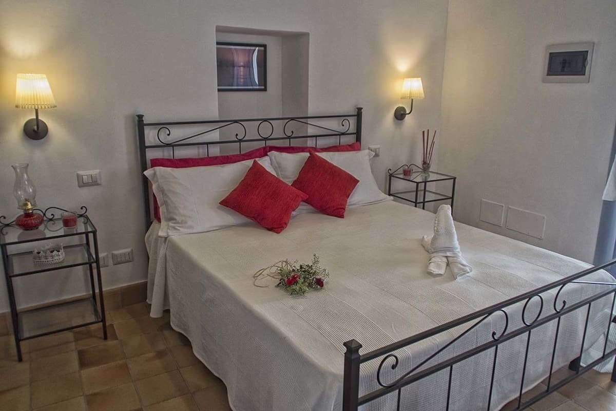 A neatly made bed with white and red bedding, two bedside tables with lamps, and a small decorative vase on the left table.