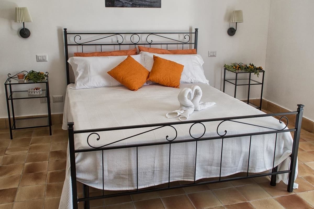 A neatly made bed with white and orange bedding, a decorative towel, and a painting above it.