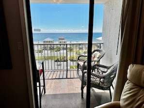 A balcony with a view of the ocean, a chair, and a table.