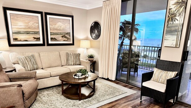 Sala de estar com sofá, poltrona, mesa de centro e vista para o oceano através de uma porta de vidro deslizante.
