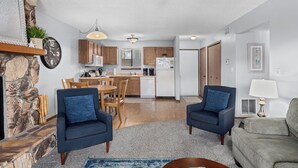 Een moderne woonkamer met een stenen openhaard, een eethoek met houten meubels, een keuken met houten keukenkastjes, en een plafondventilator.