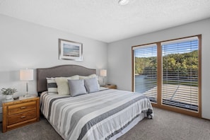 Une chambre à coucher avec un grand lit, deux tables de chevet, une commode, une fenêtre avec des stores et un tableau encadré au mur.