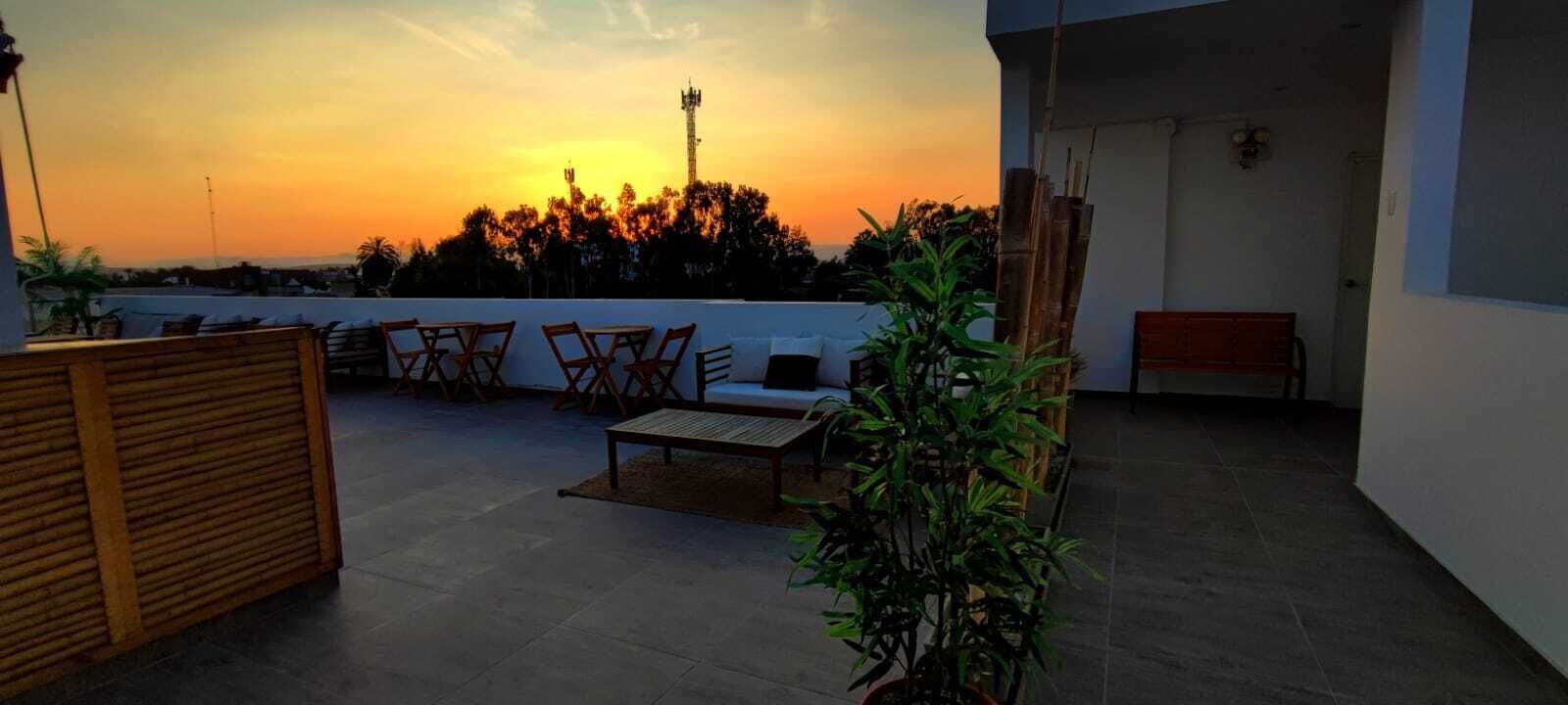 Terraza en la azotea con vista al atardecer, muebles de madera y plantas en macetas.