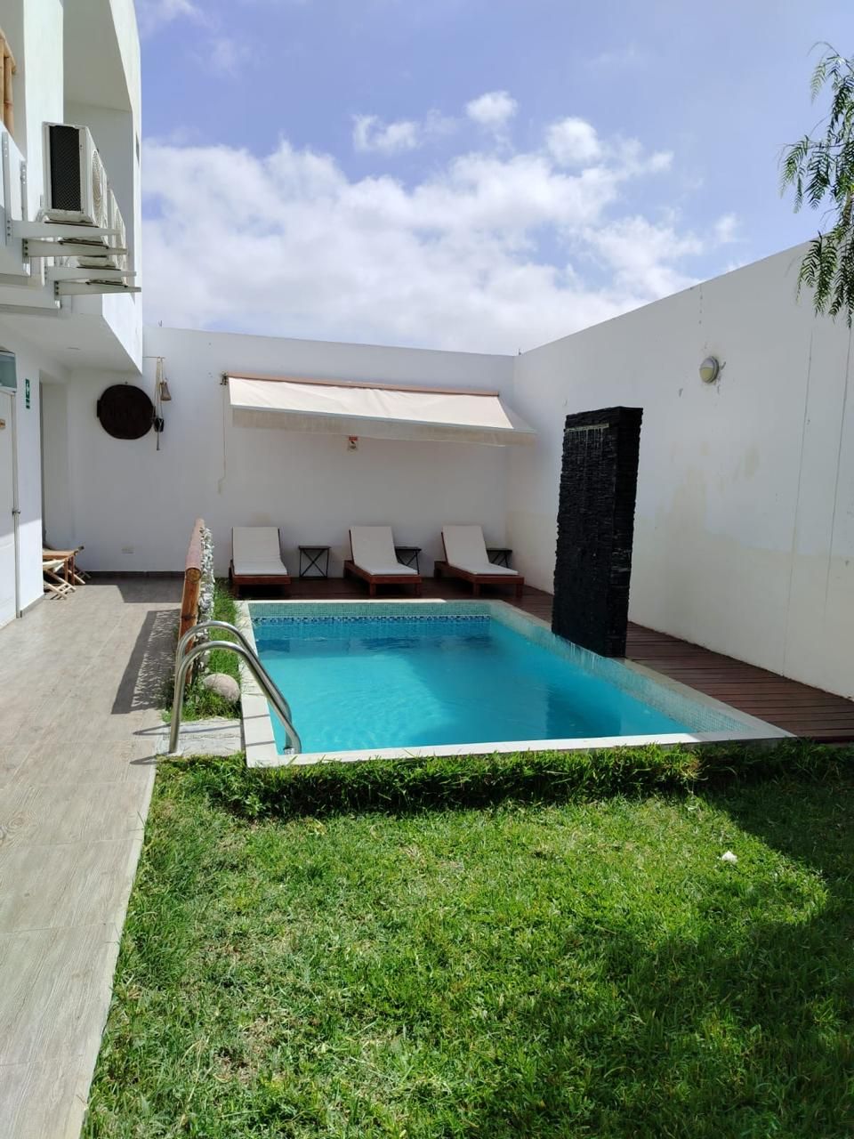 A modern outdoor pool area with a clear blue pool, a wooden deck, and a seating area with lounge chairs.