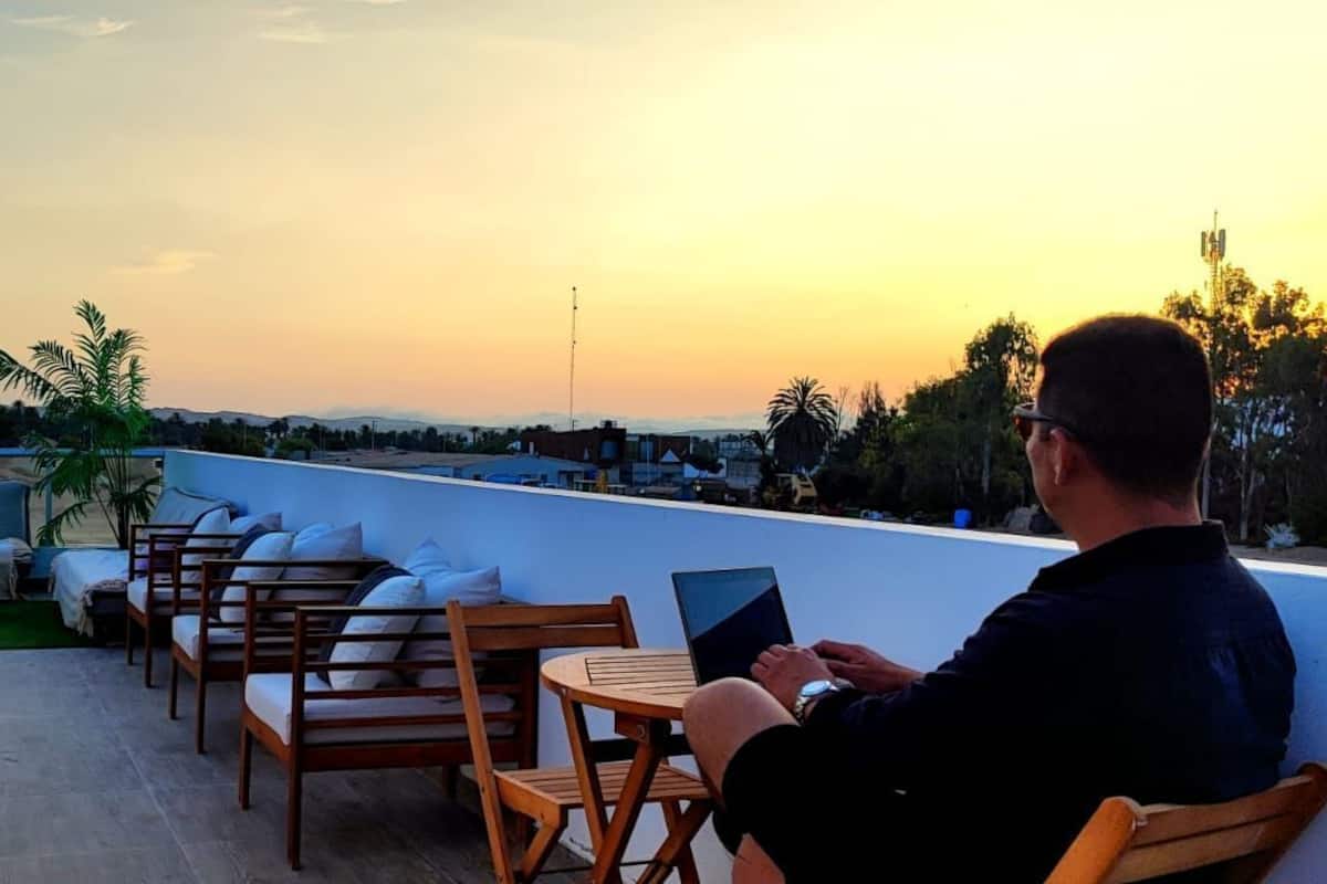 A rooftop terrace with wooden furniture, a laptop, and a sunset view.