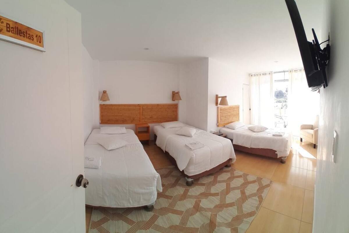 A hotel room with three beds, a wooden headboard, a patterned rug, and a television mounted on the wall.
