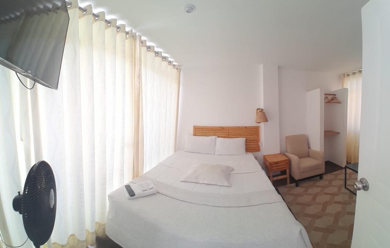 Una habitación de hotel con una cama, una silla, un escritorio y un ventilador.