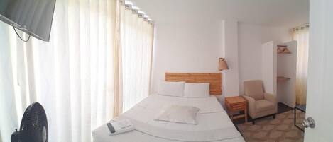 Una habitación de hotel con una cama, una silla, un escritorio y un ventilador.
