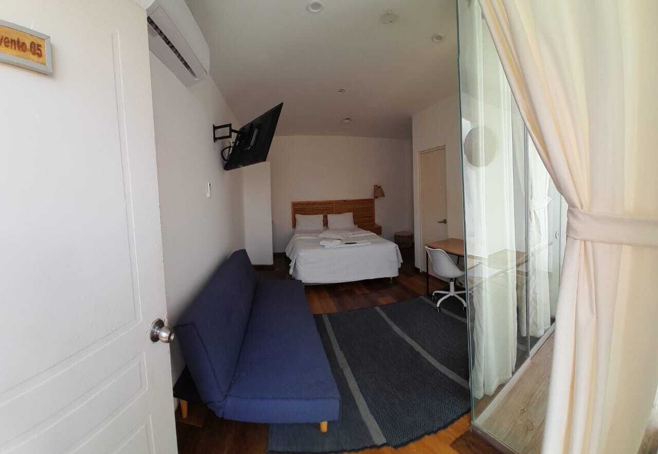 A bedroom with a bed, a sofa, a desk, and a TV mounted on the wall.