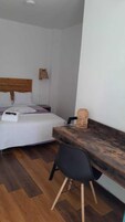 Un dormitorio con cama, mesita de noche, silla y escritorio con lámpara.