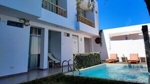 A modern building with a swimming pool, outdoor seating, and a balcony with plants. - Paracas Guest House (Paracas)
