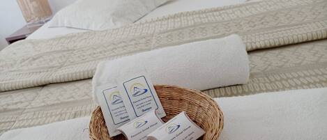 A neatly made bed with white linens and a woven basket containing toiletries.